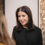 A woman in a black dress and with dark hair, Sotheby's Director Brandei Estes, converses with another woman.