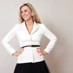 Author Christina Makris, dressed in a white jacket and black skirt, exuding elegance and style.