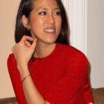 A woman, Harper's Bazaar's features director Helena Lee, sits gracefully on a couch in a striking red dress.