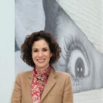 Mollie Dent-Brocklehurst, CEO of Superblue, stands poised in a camel coloured jacket and scarf against an artistic backdrop.