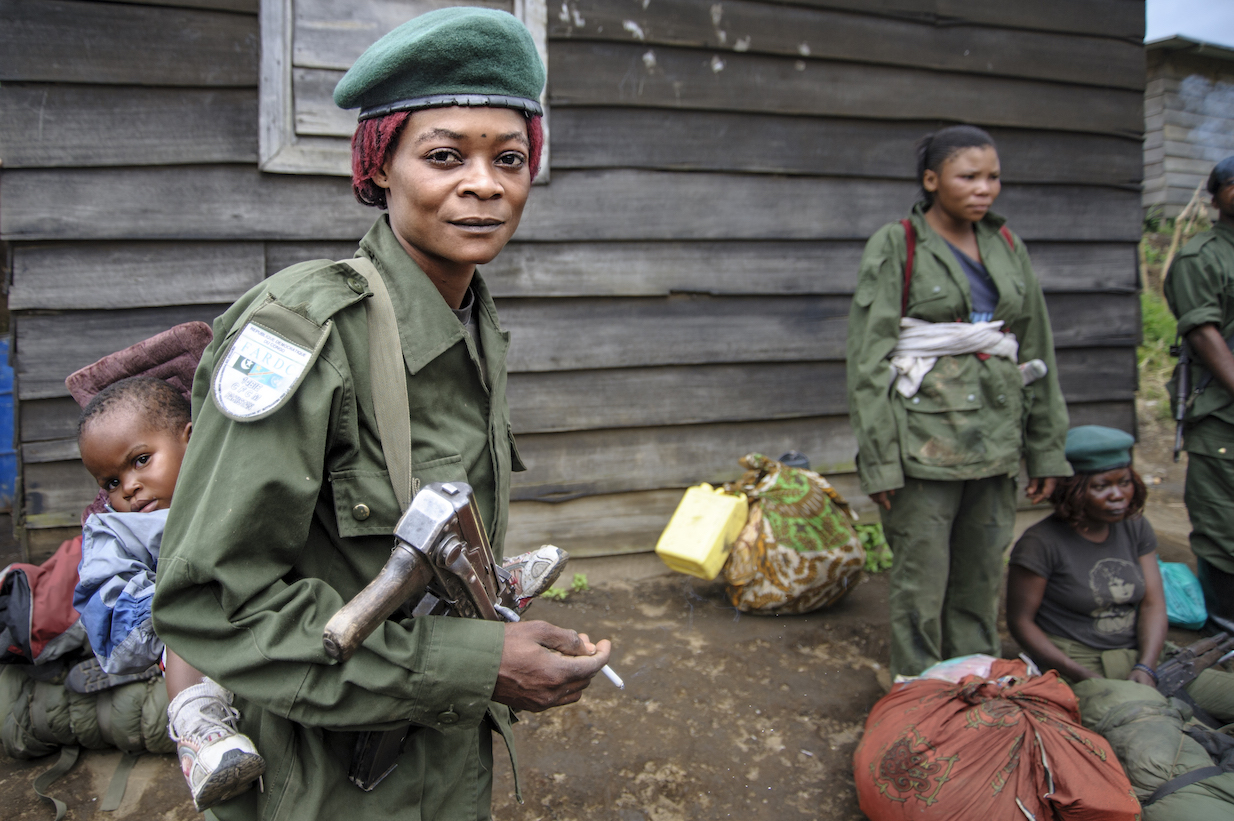The Wick - A Congolese soldier pauses for a cigarette while walking to a new post carrying her  weapon and her two-year old daughter.  Mushake, Democratic Republic of Congo. January 26, 2008
