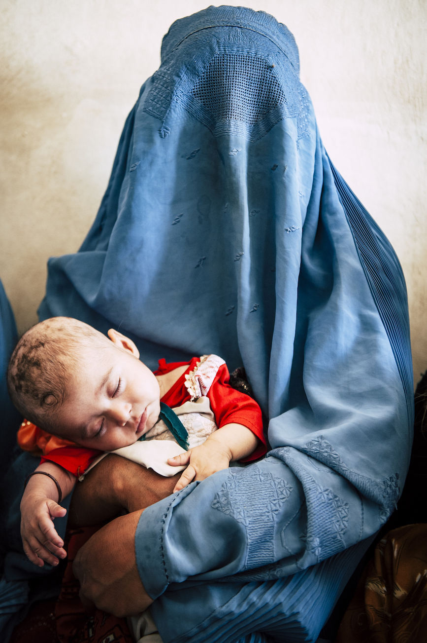 The Wick - An Afghan woman holds her newborn baby as she waits at a child and maternal health clinic in the outskirts of Herat, Afghanistan. August 20, 2013. Despite advances in women’s rights, Afghanistan remains a deeply conservative country and most women continue to wear the burqa and reluctantly visit doctors.