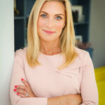 A woman with blonde hair, TalkTV Royal Editor, Sarah Hewson, wears a pink top and smiles warmly at the camera.