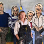 A woman, artist Freya Jones, stands before a family painting reflecting on the themes of connection and belonging depicted.