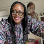 A woman, collage artist Sharon Walters, wears glasses and a floral top and smiles for the camera.