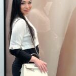 A woman, entrepreneur Shanyan Yoder, smiles for a picture wearing black trousers and a white jacket and handbag.