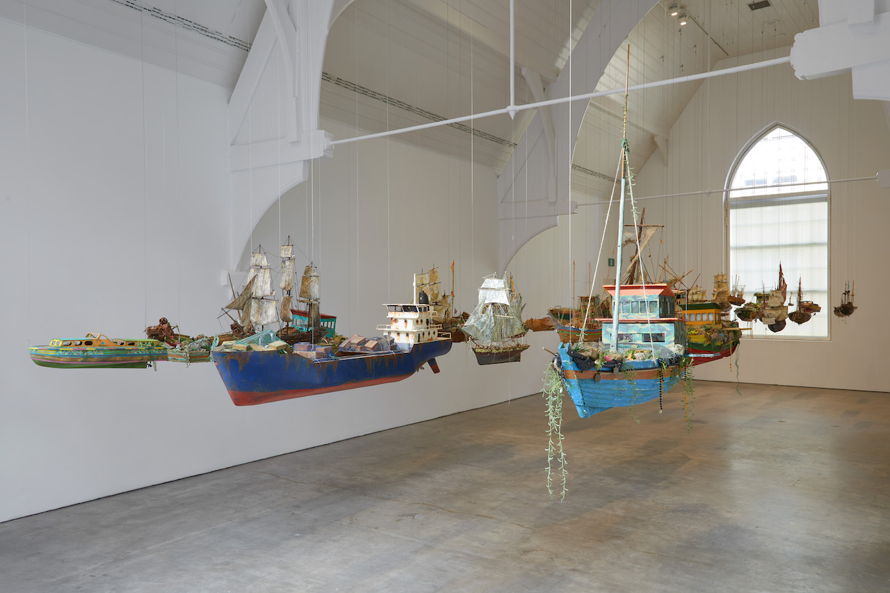 The Wick - Hew Locke RA, Armada, 2017–19
Installation: wood, textile, metal, string, plastic, rubber, paper and paint, dimensions variable
Tate. Purchased with assistance from Tate International Council and with Art Fund support 2021
Courtesy the artist and Ikon Gallery. Photo: Stuart Whipps
© Hew Locke. All Rights Reserved, DACS 2024
