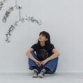A woman with long dark hair, artist Georgina Odell, sits in a white room wearing jeans and black converse while looking up at some silver sculptures.