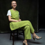 A woman with short hair, Paul Smith's Foundation Director Martha Mosse, sits on a chair wearing a vivid green trouser suit and snakeskin heels.