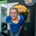 Woman in blue shirt standing in front of mirror.