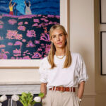Louisa Preskett, entrepreneur and founder of Maison Margaux, stands in front of a captivating painting, with her hands in her pockets.