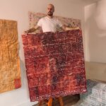 Bald white man standing on a stool holding a red artwork by Gommie