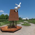 Photo of a large metal roof sculpture in a garden – Hauser Wirth Somerset – with a white abstract bunny by Phyllida Barlow seated on top.