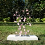 Metal sculpture with pink organic structures, titled "Sand" by Juliana Cerqueira Leite, on a pillar in a park