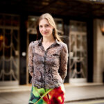 Brunette young woman, Daria Blum, standing outside in front of Claridge's Hotel, wearing an animal printed button down shirt and colourful green and red skirt