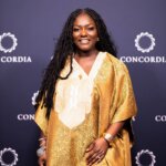 A woman, Dentaa Amoateng MBE, wears a gold long dress and various pieces of jewellery at an event.