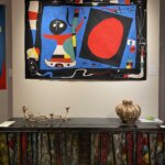 Colourful tapestry by Miro above a a vintage table with two gold objects