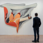 A man in a suit stands admiring a piece of art on a white wall at Art Basel depicting a woman's lips and hand holding a cigarette with grey smoke.
