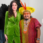 Brunette white woman on left in lime green suit and Brazilian Amazonian man in colourful outfit on the right