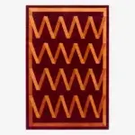 A burgundy rug by Campbell-Rey for Nordic Knots featuring orange zig zag pattern.