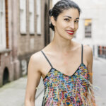 Photograph of brunette woman with red lipstick, Caroline Issa, standing outside in a colorful dress