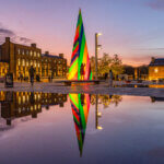 Photograph of large triangle with colourful diagonal stripes, by Liz West, in front of water at Granary Square in Kings Cross.
