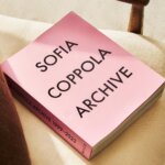 Pink book titled Archive by Sofia Coppola sitting on a beige chair.