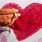 Photograph by Martin Parr of an old woman's hand holding a cigarette who is wearing a light pink t-shirt with a pink heart.