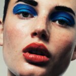 Woman wearing bright blue thick eyeshadow with bright red lipstick.