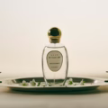 Perfume bottle with a gold lid and a white label, sitting on a silver tray with white flowers.