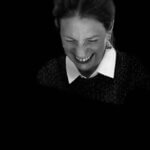 Black and white photograph of a woman, Hannah Barry, wearing a white shirt and black jumper. The woman is laughing with her eyes closed and her hair is in a ponytail.