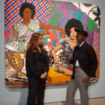 Two women, standing in a gallery, talking in front of a colourful artwork.