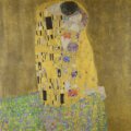 Yellow painting, The Kiss, by Gustav Klimt of a man and a woman kissing. The man has black hair and the woman brown.