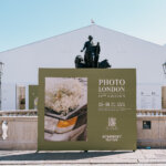 A photograph of a green sign in front of a statue and white tent