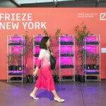 A pink billboard with 'Frieze New York' written on it with a person in a pink dress walking in front