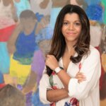 A woman with brown hair standing in front of colourful abstract painting