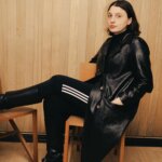 A woman wearing black tracksuits and a leather jacket sitting on a chair