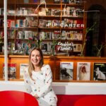 A woman sitting on a red bench outside a newsagent