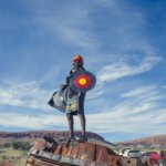 A Black person standing on a rock wearing a superhero costume
