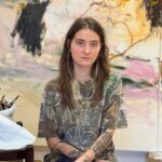 A young woman with brown hair standing in front of a painting