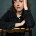 A woman with brown hair sitting on the back of a chair
