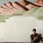 A photograph of a person sitting in front of a photograph of a landscape