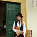 A woman wearing a white shirt and black waistcoat and hat, holding a chicken
