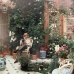 Cecil Beaton sitting in his indoor Winter Garden at Reddish House with his pet pug