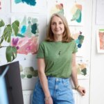 A woman wearing blue jeans and a green top standing in front of a wall