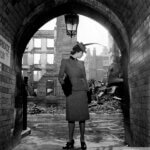 A black and white photograph of a woman standing in a door way