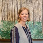 A woman with short blonde hair standing in front of a painting