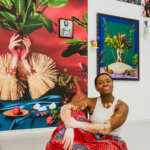 A woman sat on the floor in a red skirt in front of paintings