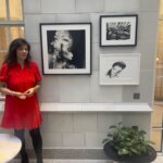 A woman wearing a red dress standing next to three black and white artworks