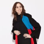A woman with brow hair wearing a black, red, and blue jacket